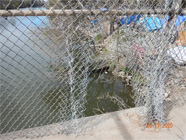 Hole in chain link fence of Smith Canal walking bridge showing shortcut to homeless encampment along the side of the canal.  Blue tarps and debris of encampment - Date of 03.11.2020 shows at the bottom of the photo