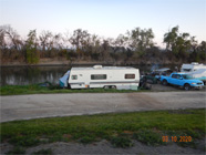 Image #1 Homeless encampment along the Sacrameto River in Knights Landing. Pictured are several trailers, golf cart, truck, tents, boat with smoke coming up from an area in the background.