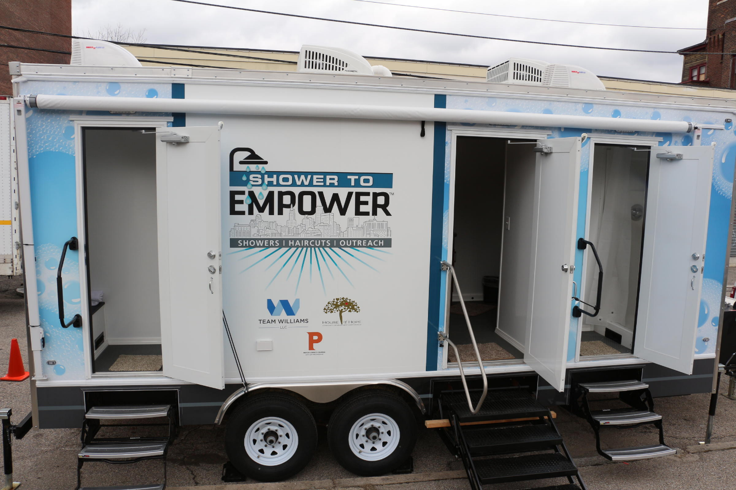 image of a mobile sanitation unit with words SHOWER TO EMPOWER on side of white trailer with 3 sets of steps going up to open doors