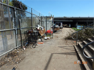 Smith Canal levee and bridge with canal and concrete steps of walking bridge off to the right. Five different shopping carts lined up with debris along chain link fence to the right. Tent setup in background to the left under the driving bridge and canal water seen to the right. - Date of 03.11.2020 shows at the bottom of the photo