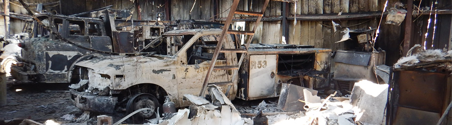 Firestation after it burned down.  Emergency vehicles white from ash and shell of a garage leftover.