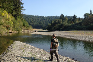 Man walking along stream and carrying monitoring equipment