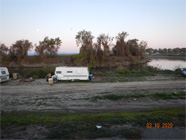 Smith Canal levee and bridge with canal and concrete steps of walking bridge off to the right. Five different shopping carts lined up with debris along chain link fence to the right. Tent setup in background to the left under the driving bridge and canal water seen to the right. - Date of 03.11.2020 shows at the bottom of the photo