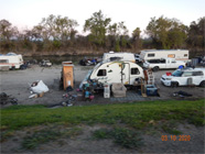 Hole in chain link fence of Smith Canal walking bridge showing shortcut to homeless encampment along the side of the canal.  Blue tarps and debris of encampment - Date of 03.11.2020 shows at the bottom of the photo