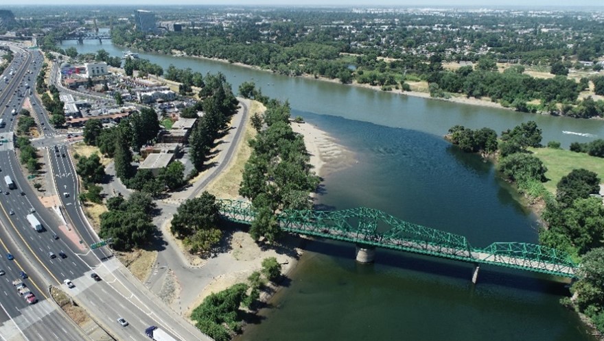 aerial view of the lower american river where it meets the sacramento river at discovery park, green bridge going over river, highway and cars next to river