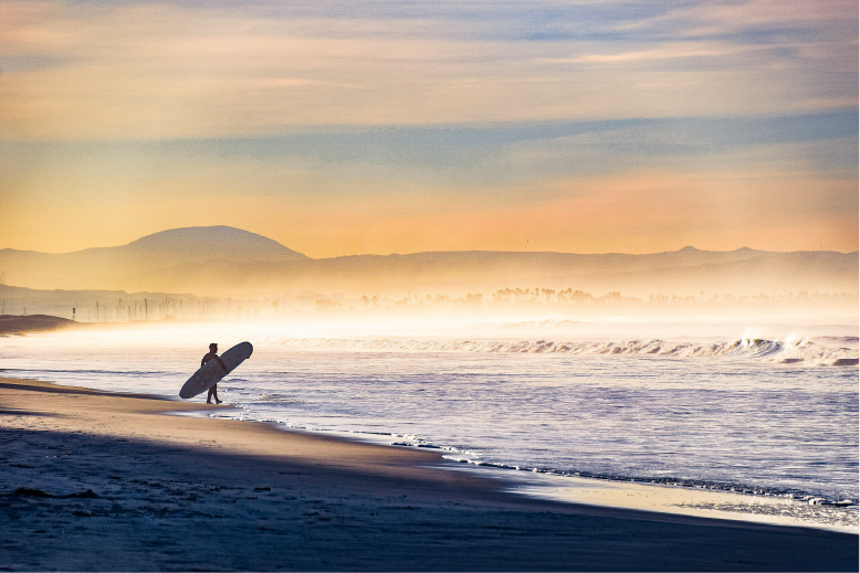 Sunset at the beach with a silhoutte of a surfer on the shore